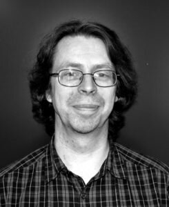 Foto på Lars Östvall. Man i glasögon och rutig skjorta och halvlångt mörkt hår.