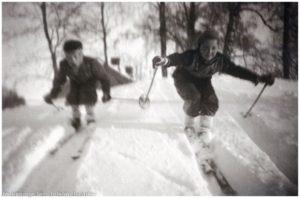 Två barn åker skidor nerför backe.