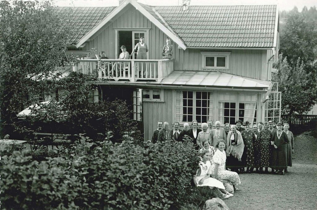 En grupp kvinnor på semesterhemmet ”Mors Vila” vid Vista kulle (Bergsäter, Skärstad). Byggnaden är omgiven av buskar och träd. Framför verandan poserar en stor grupp kvinnor, även på balkongen ses några av gästerna.