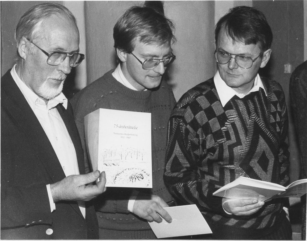 Tre män håller upp jubileumsskrift.
